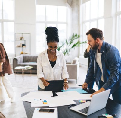 Group of multiracial businesspeople standing at wooden table with papers laptop and smartphone while discussing business startup in modern workshop together