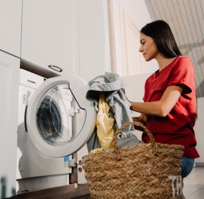 Young hispanic brunette woman putting clothes at washing machine while doing laundry at home